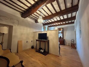 A room with exposed wooden beams, a television on a stand, a chandelier, and a chair.