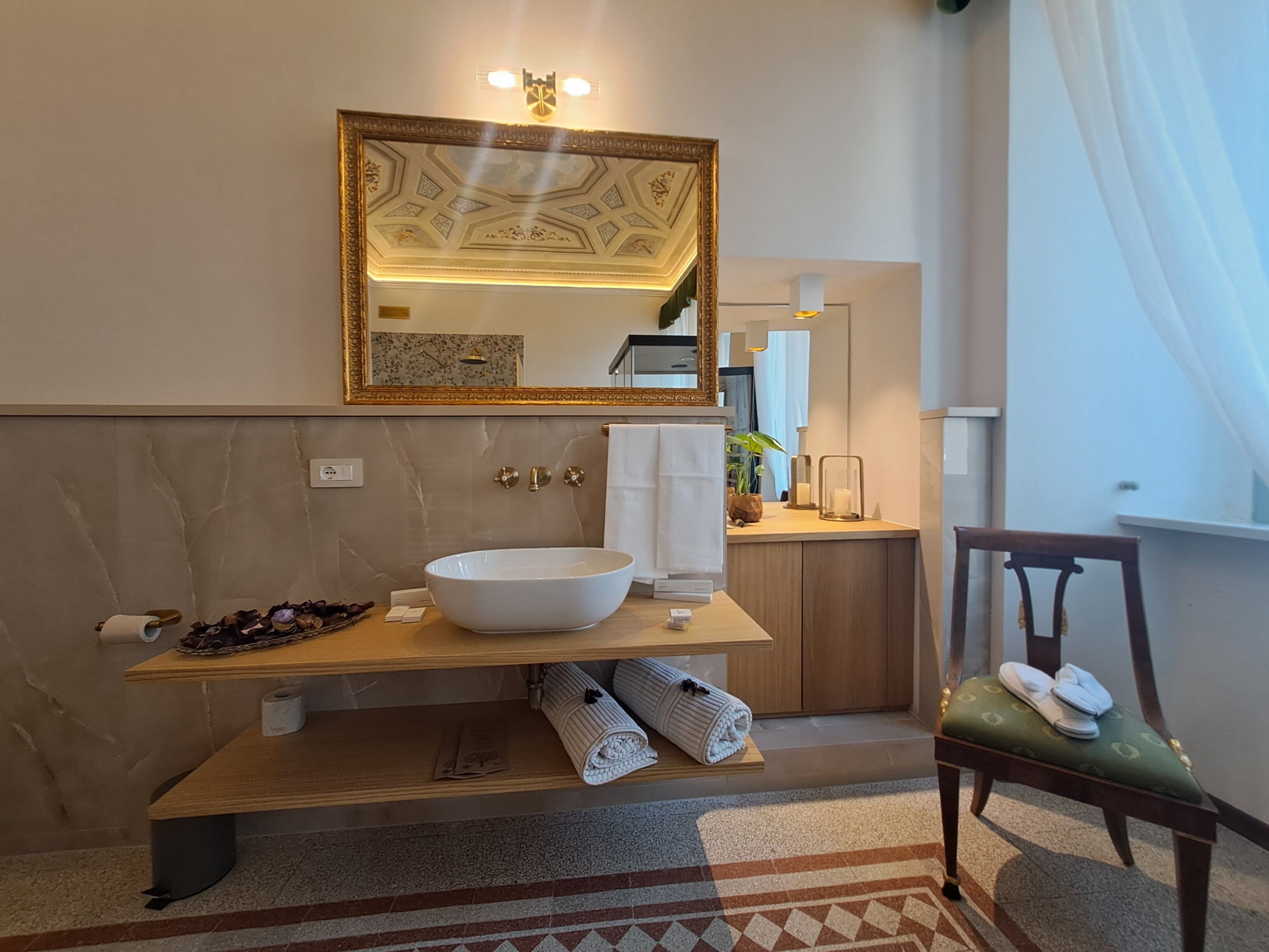 A bathroom with a large mirror, a vessel sink, a wooden vanity, a towel rack, and a chair.