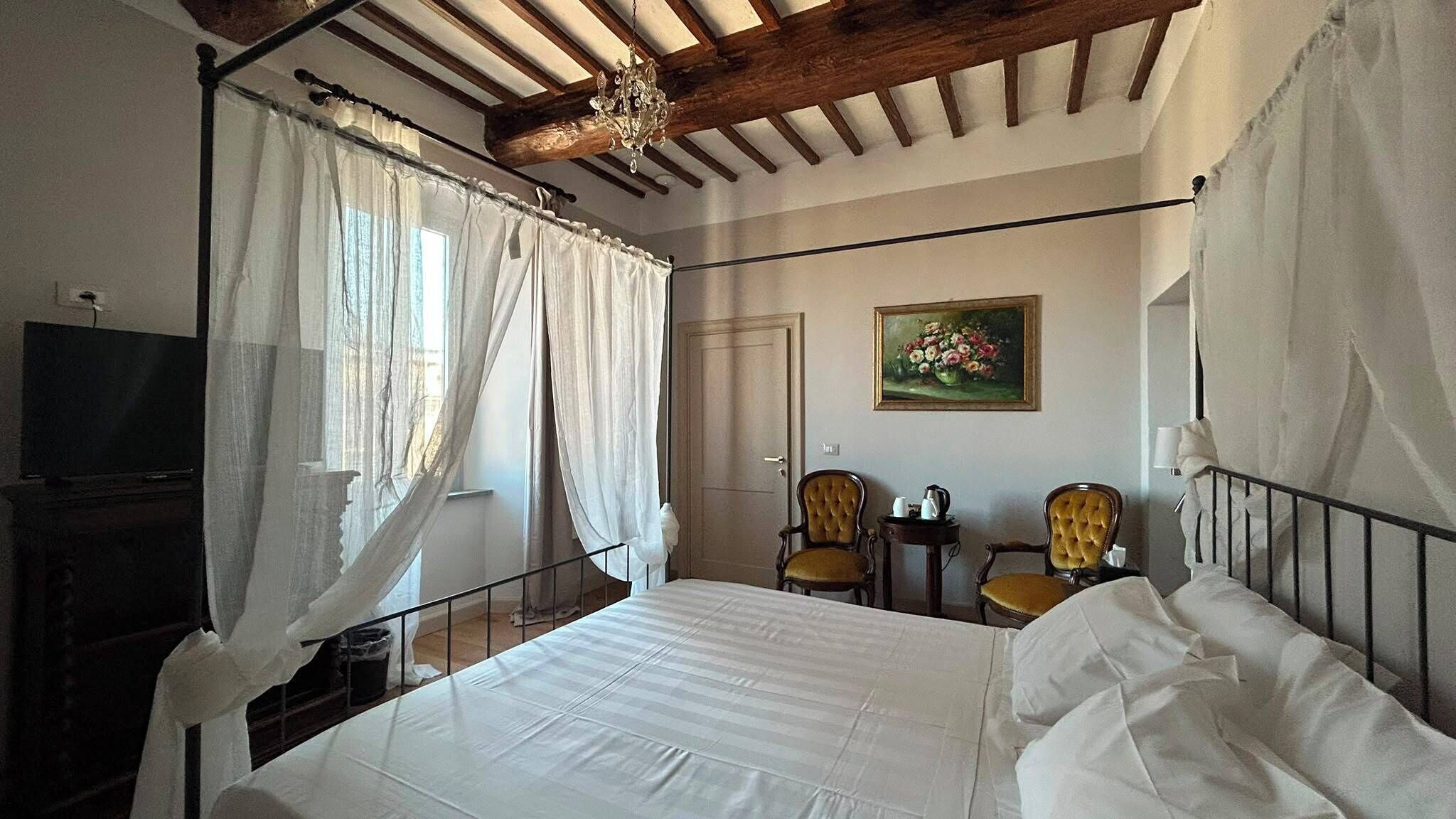 Ein Schlafzimmer mit Himmelbett, Fernseher, zwei Sessel, einem Gemälde an der Wand und einer Chandelier.
