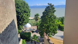 A balcony with a view of a lake, trees, and a white structure. - Garden Palace Hotel (Castiglione del Lago)