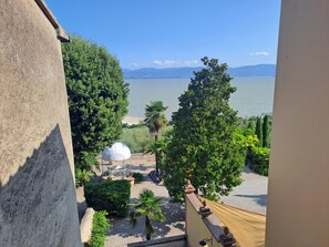 A balcony with a view of a lake, trees, and a white structure.