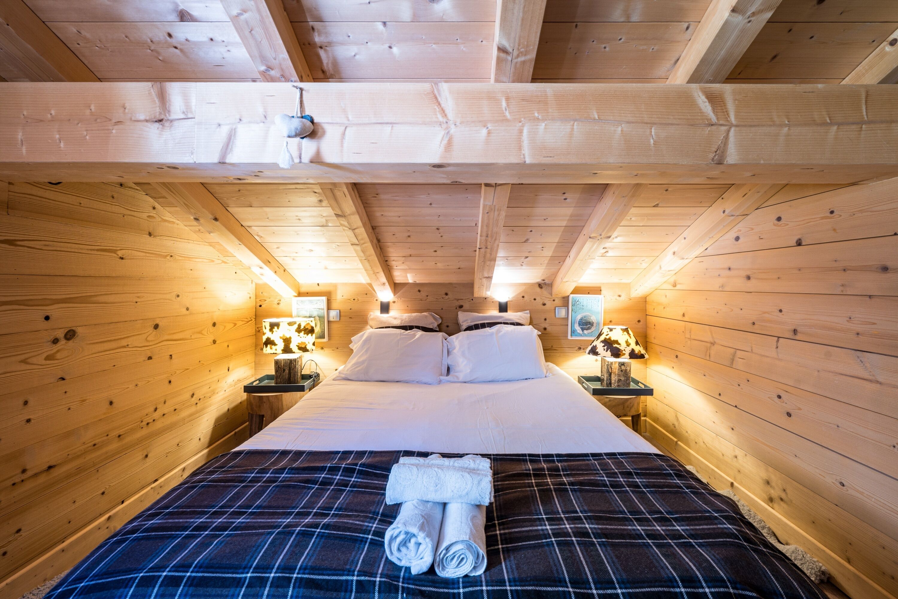 Un dormitorio de cabaña de madera con una cama, dos mesitas de noche y un cabecero.