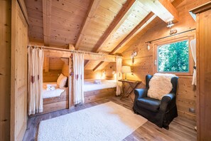 A wooden cabin with a loft bedroom, a cozy chair, and a large window. - Lodge Le Chevreuil - Piscine, jacuzzi et sauna (Le Grand Bornand)