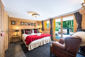 A bedroom with a bed, a chair, a wooden wall with framed pictures, a window, and a view of the outdoors. - Lodge Le Chevreuil - Piscine, jacuzzi et sauna (Le Grand Bornand)
