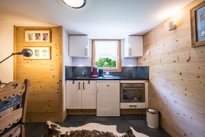 A compact kitchen with wooden cabinetry, a window, and a view of greenery outside. - Lodge Le Chevreuil - Piscine, jacuzzi et sauna (Le Grand Bornand)