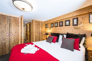 Ein Hotelzimmer mit Holzvertäfelung, einem Bett mit rot-grauen Bettwaren, einem Kopfteil mit gerahmten Bildern und einem Holzschrank.