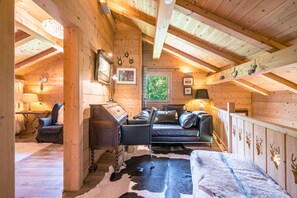 A cozy cabin interior with a wooden ceiling, a leather sofa, a cowhide rug, and a rustic wooden cabinet. - Lodge Le Chevreuil - Piscine, jacuzzi et sauna (Le Grand Bornand)