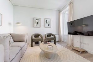 Ein modernes Wohnzimmer mit Sofa, zwei Sesseln, einem Couchtisch, einem Flachbildfernseher und Kunstwerken an der Wand.