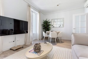 Ein modernes Wohnzimmer mit Flachbildfernseher, einer Essecke mit Tisch und Stühlen, einem großen Spiegel und einem Sofa.
