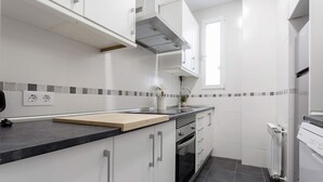 A kitchen with white cabinets, a black countertop, a window, and a tiled backsplash. - Genteel Home Reina Sofia IV (Madrid)
