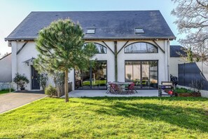 Ein modernes, zweistöckiges Haus mit großem Vorgarten, einem Essbereich mit Gartenmöbeln und einer Garage.