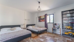 A bedroom with two beds, a window with curtains, a shelf with toys, and a wall with a colorful painting. - 180-square-meter house · Pool table · Air conditioning · Garden · Tours (Chambray-lès-Tours)