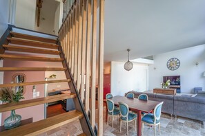 Ein modernes Interieur mit einer Holztreppe, einem Essbereich mit blauen Stühlen und einem Wohnzimmer mit Sofa und Fernseher.