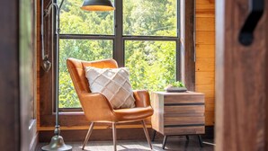 A room with a large window, a leather chair, a wooden cabinet, and a floor lamp. - Cloud Haven Retreat | Views, Hot Tub + Games (Gatlinburg)