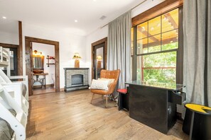 A modern living room with a fireplace, a comfortable chair, and a large window offering a view of greenery. - Cloud Haven Retreat | Views, Hot Tub + Games (Gatlinburg)