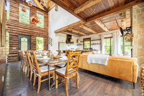 A rustic interior with a wooden dining table, chairs, a sofa, and a stone wall. - Cloud Haven Retreat | Views, Hot Tub + Games (Gatlinburg)