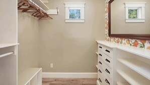 Um closet espaçoso com prateleiras de madeira, um espelho e duas janelas.