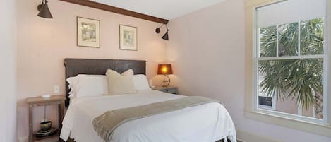 Une chambre à coucher avec un lit, des tables de chevet, une lampe et une fenêtre donnant sur des palmiers.