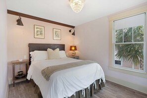 Ein Schlafzimmer mit Bett, Nachttischen, einer Lampe und einem Fenster mit Blick auf Palmen.