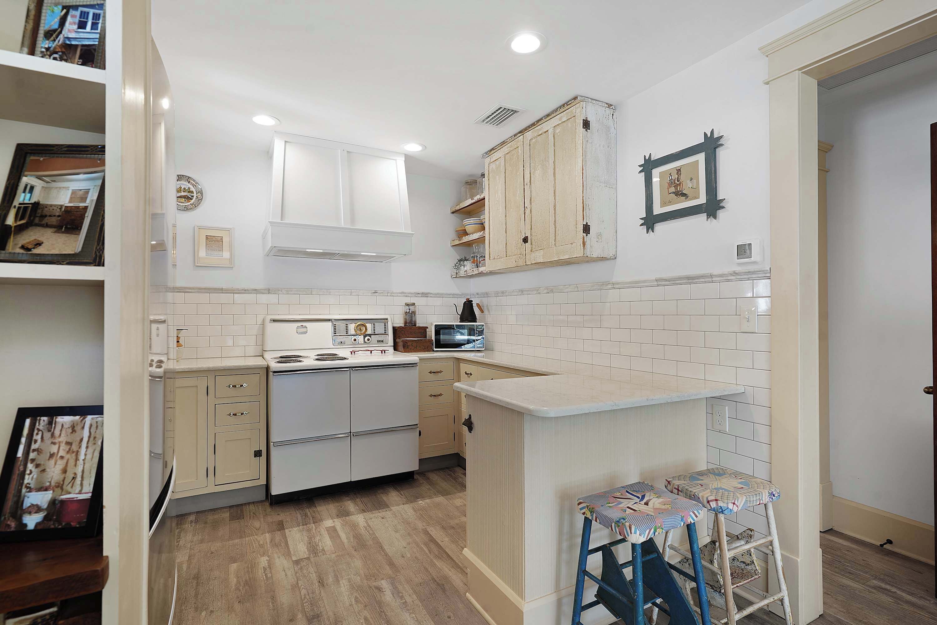 A kitchen with white cabinets, a stove, a microwave, and a small bar area with stools.