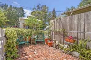 Eine Terrasse aus Ziegelsteinen mit Holzzaun, einem grünen Stuhl und Topfpflanzen.