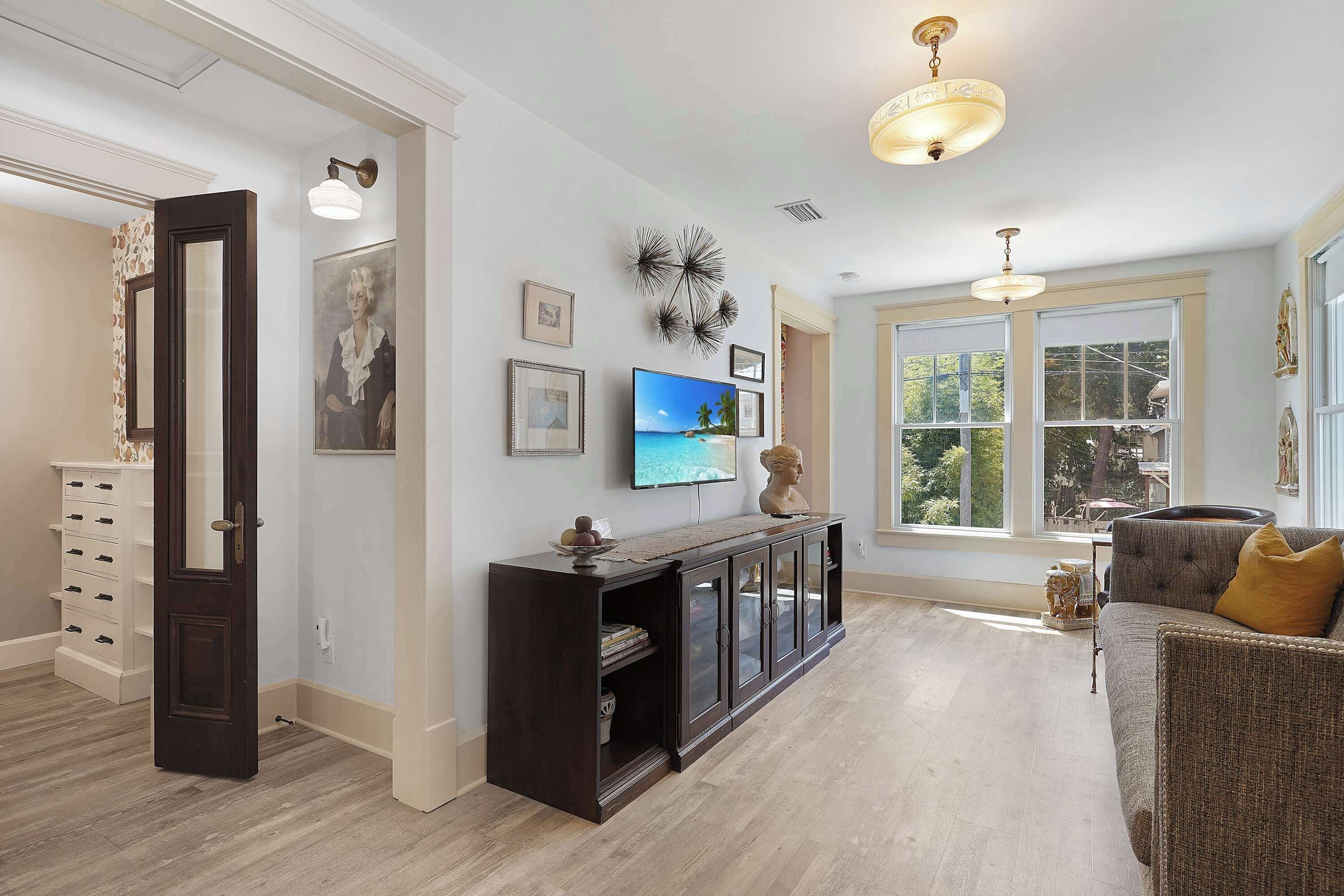 A spacious living area with a dark wood console table, a flat-screen TV, and a large window offering a view of the outdoors.
