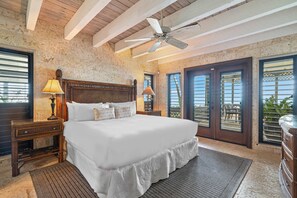Un dormitorio con una cama grande, dos mesitas de noche, un ventilador de techo y vistas al exterior a través de un ventanal corredera.
