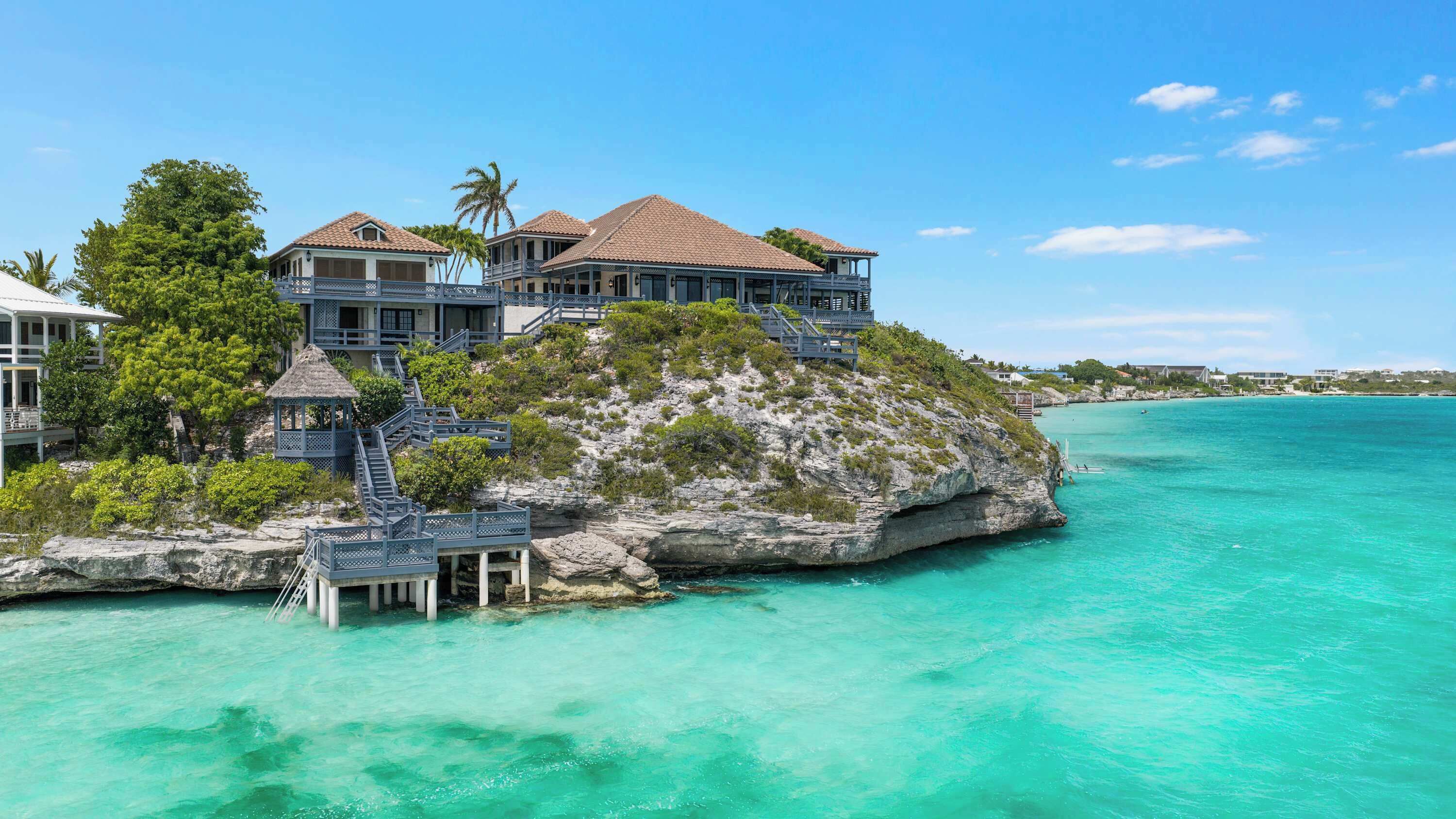 A beachfront property with multiple buildings, a staircase leading to a deck, and clear turquoise waters.