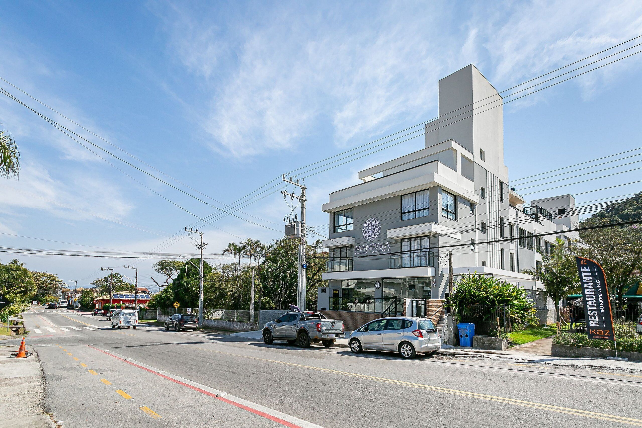 Edifício moderno com telhado plano e grandes janelas, situado em esquina com carros estacionados na frente.