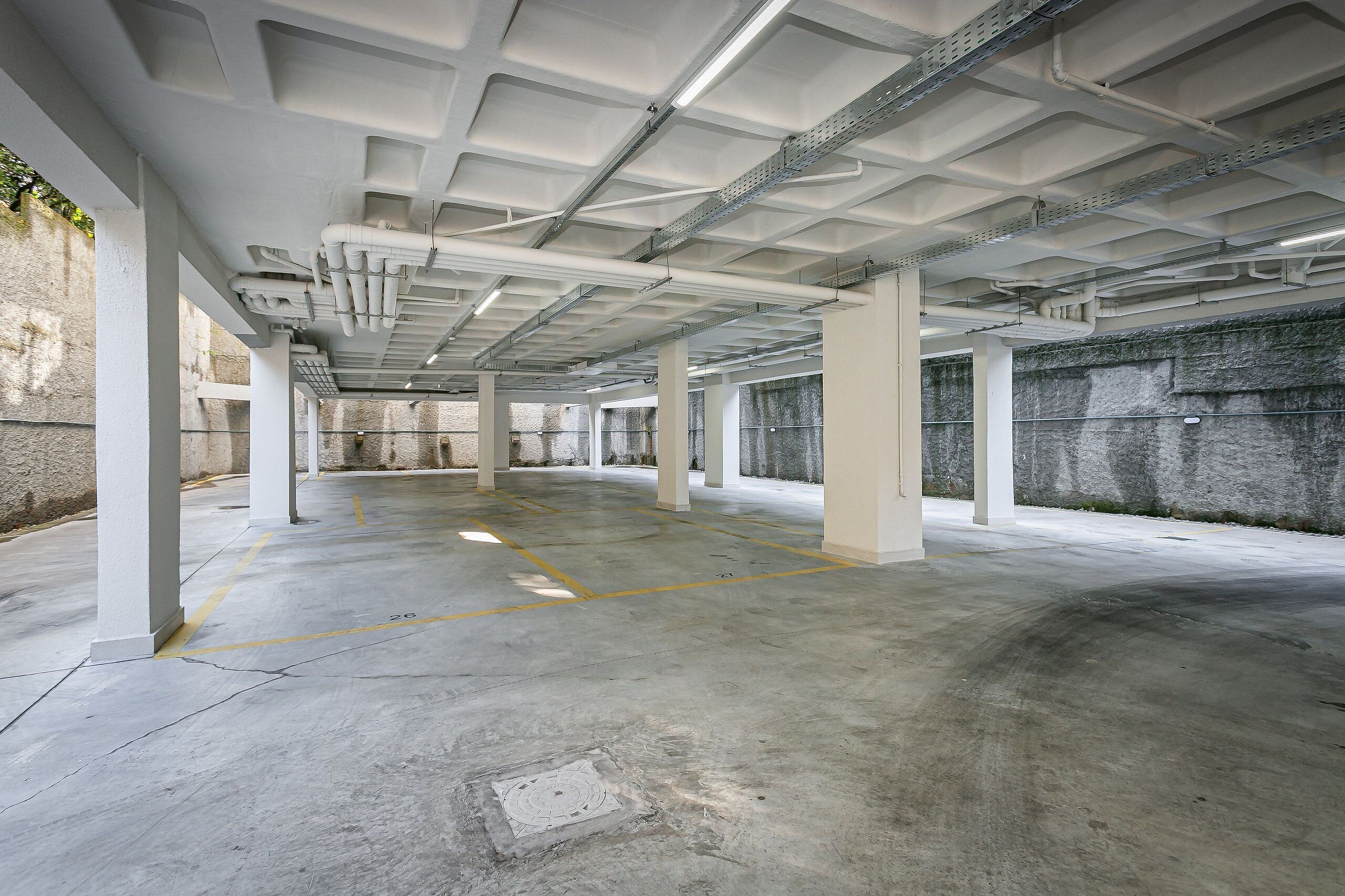 Garagem de estacionamento vazia com piso de concreto, pilares brancos e tubulações no teto.