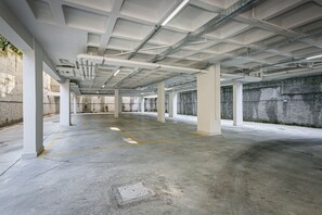 Garagem de estacionamento vazia com piso de concreto, pilares brancos e tubulações no teto.