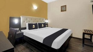 A hotel room with a bed, bedside table, lamp, and a small stool.
