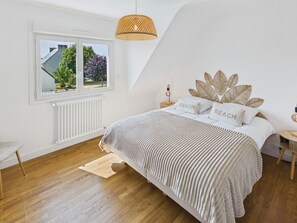 Ein Schlafzimmer mit Bett, Fenster, Heizkörper, Holzboden und einer Pendelleuchte.