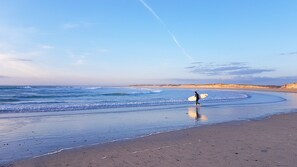 Ein Strand mit einer Person, die einen Surfbrett trägt.