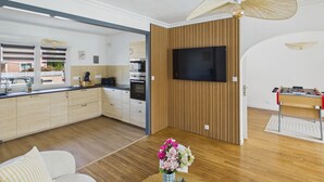 Una cuina moderna amb armaris de fusta, forn integrat i un gran televisor de pantalla plana penjat a la paret.