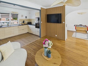 Eine moderne Küche mit Holzausstattung, einem integrierten Backofen und einem großen Flachbildfernseher an der Wand.
