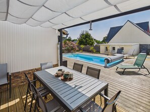 Eine Außenpatio mit Pool, Holzterrasse und überdachter Sitzgruppe.