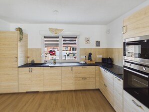 A modern kitchen with wooden cabinets, a black countertop, a built-in oven, and a window with a view of the outside. - House for 6, pool, boules & foosball (Plomeur)