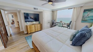 Een slaapkamer met een groot bed, een televisie, een bureau met stoel en uitzicht op de zee.