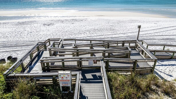 Een houten looppad dat naar een strand leidt, met een bord waarop een waarschuwing voor sterke stroming staat.