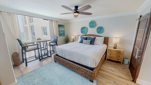 A bedroom with a large bed, a ceiling fan, a nightstand, a lamp, and a view of the outdoors. - Stunning & Renovated 2 Bedroom ST 2105 (Destin)