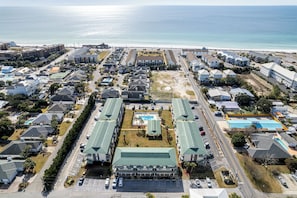 An aerial view of a coastal residential area with multiple buildings, a swimming pool, and a beach in the background. - Spacious + In A Great Location Sandprints B1 (Miramar Beach)