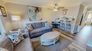 A living room with a sofa, coffee table, and a painting on the wall. - Spacious + In A Great Location Sandprints B1 (Miramar Beach)