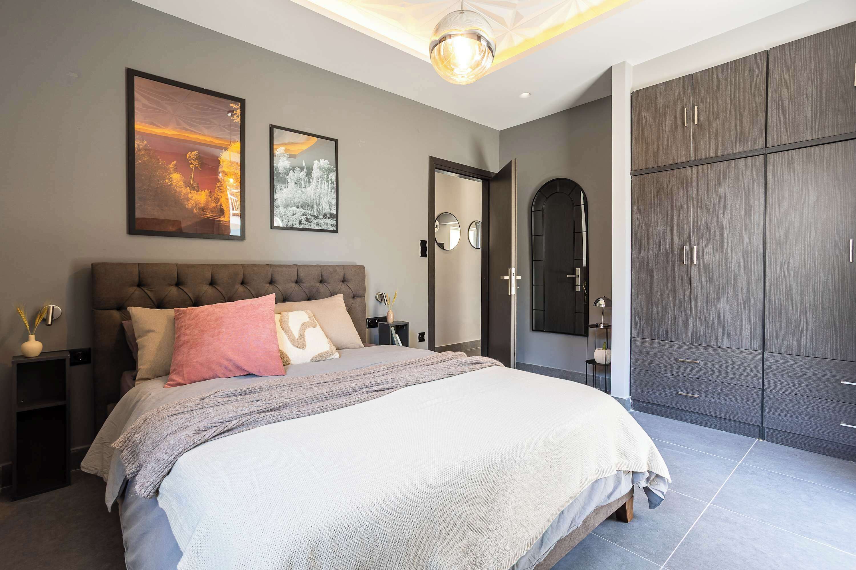 A modern bedroom with a large bed, a wardrobe, and two framed pictures on the wall.