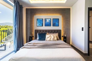 Une chambre avec un grand lit, une vue sur l’extérieur et trois tableaux encadrés accrochés au mur.