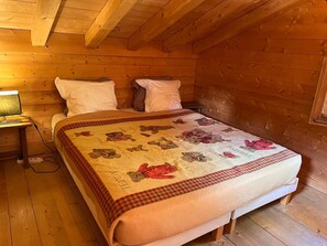Ein Zimmer in einer Holzhütte mit einem Bett, Kissen, einem Nachttisch mit Lampe und einer Bettdecke mit Bär-Motiven.