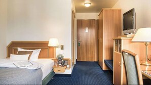 Une chambre d’hôtel comprenant un lit, une table de chevet, une lampe, une télévision et une armoire.