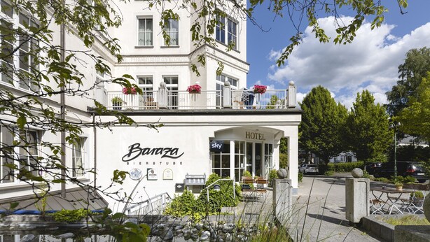 Un hôtel appelé « Baraza Bierstube », doté d’une entrée bien visible, d’un espace extérieur aménagé pour s’asseoir et d’un balcon orné de fleurs.