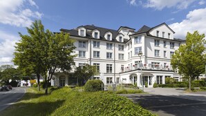 A multi-story hotel with a symmetrical facade, large windows, and a well-maintained garden in front. - Explore Lakes & Forests | Single Room | Sauna & Dining Experience (Sundern (Sauerland))