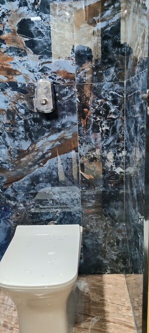 Un baño con inodoro, paredes de mármol y cabina de ducha de vidrio.